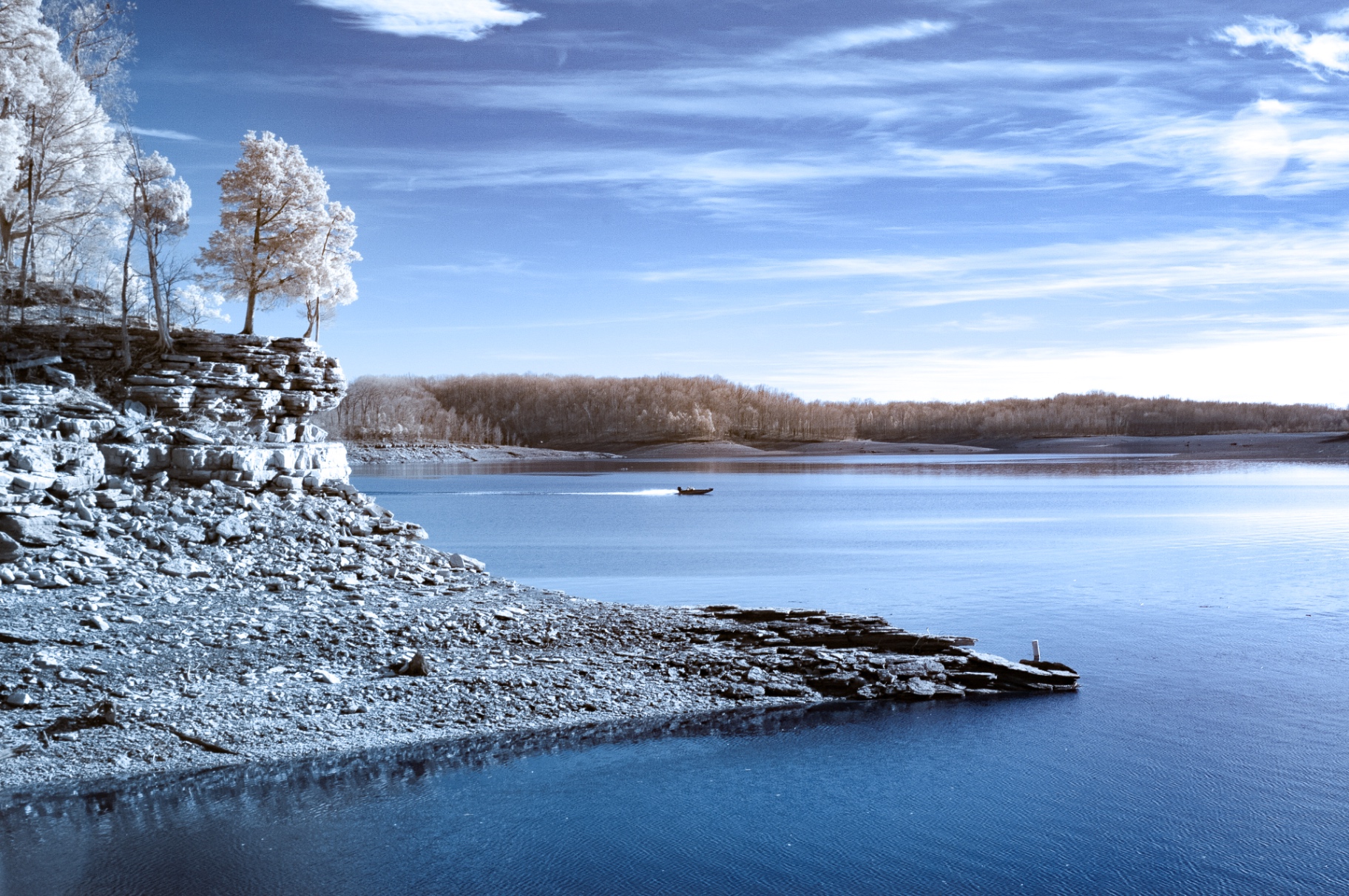 Cool blue infrared lake with a distant boat and rocky shore